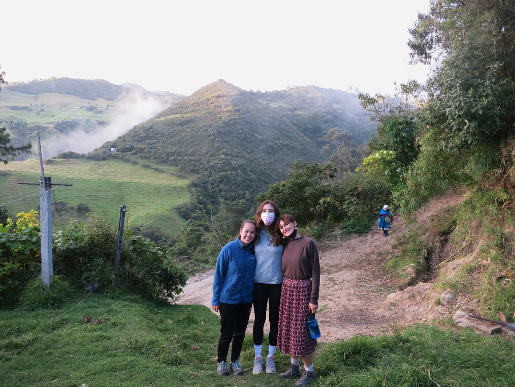 Three volunteers standing and smiling in front of hills